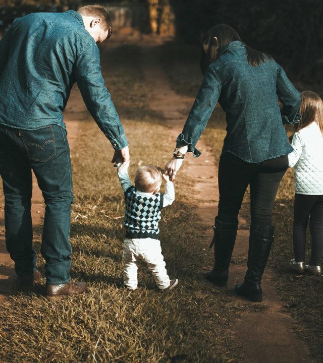 A family of four walks hand in hand on a path, enjoying a sunny day outdoors.