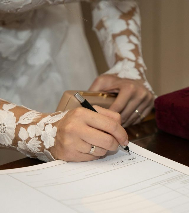 Bride in lace dress signing marriage certificate at wedding ceremony.