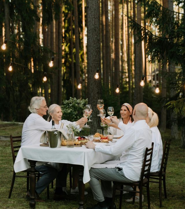 A group of friends toasting in a cheerful outdoor dinner setting surrounded by nature.