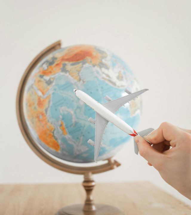 Close-up of a hand with a toy airplane in front of a globe, symbolizing travel and exploration.