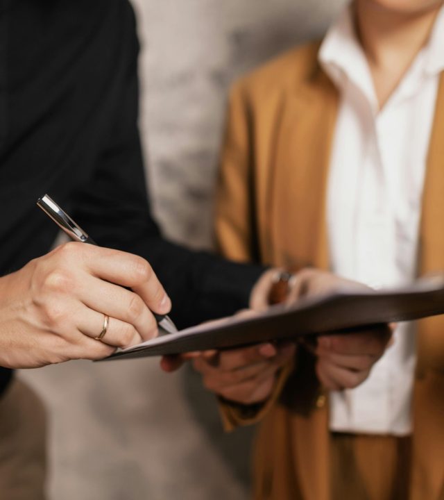 Close-up of two professionals signing a document indoors, focus on hands and pen.